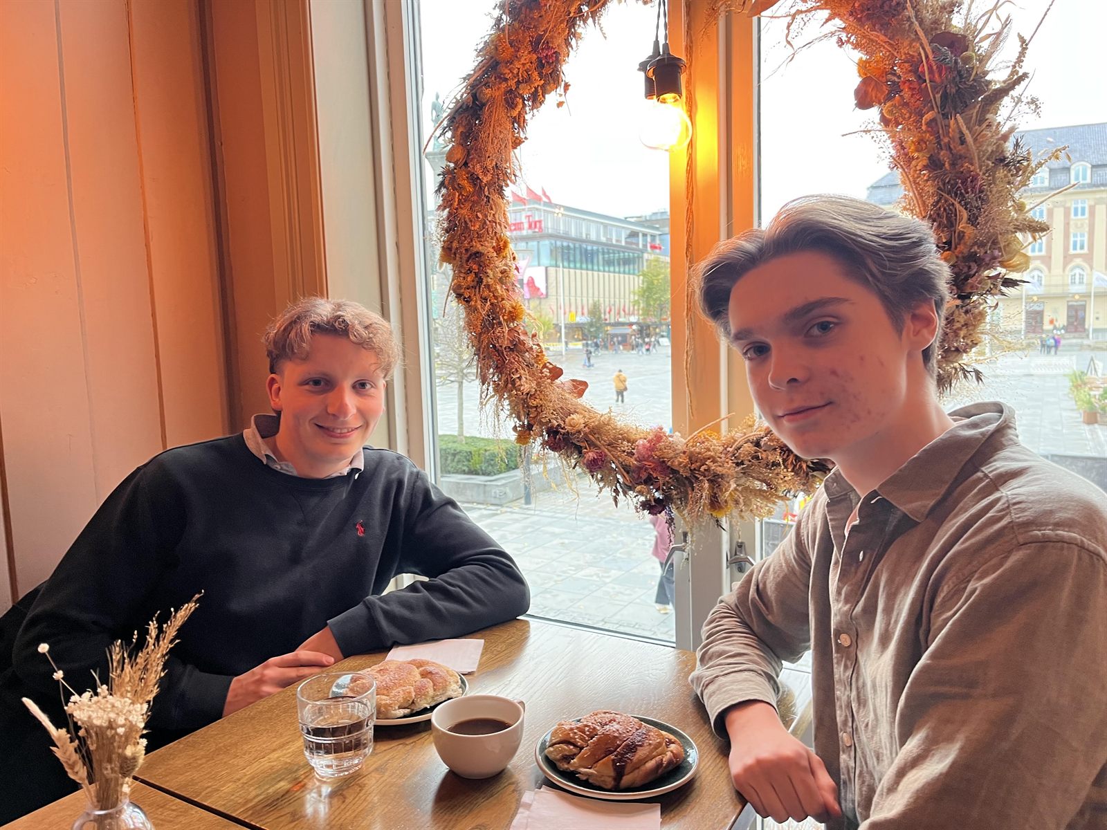 Mathias Adam (til venstre) og Oliver Andreas Brattland (til høyre) sitter ved et kafébord og smiler.